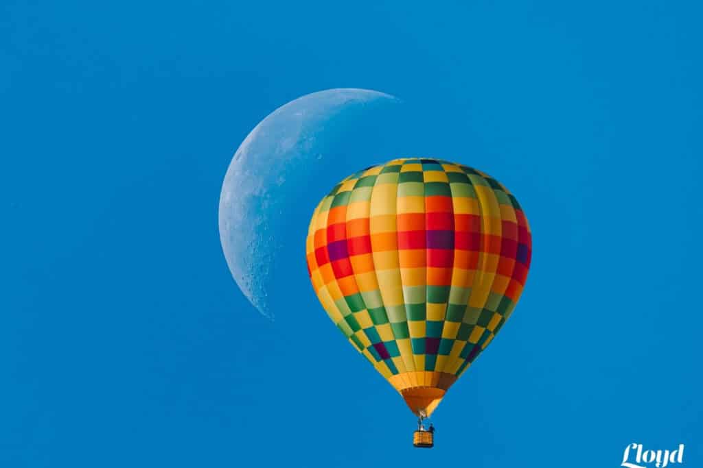 A colorful hot air balloon floating in front of the moon with a bright blue sky in the background, showcasing the beauty of capturing photos in motion.