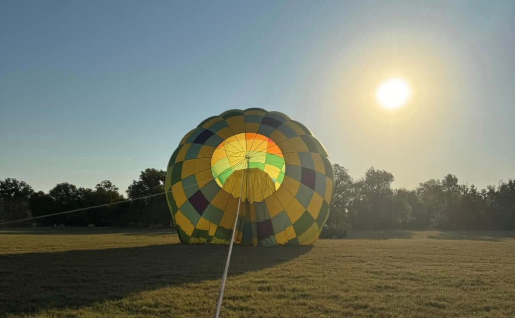 Colorful hot air balloon partially inflated on the ground at sunrise during a balloon festival.