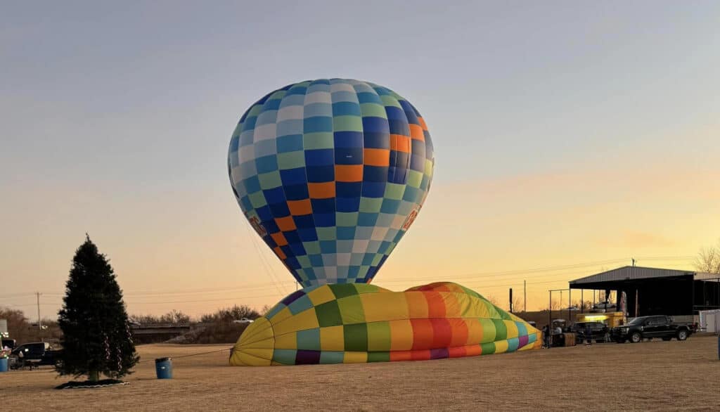 A colorful hot air balloon partially inflated on a grassy field during sunset, preparing for a balloon ride.